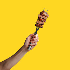 a man's hand holds pieces of roasted meat on a fork