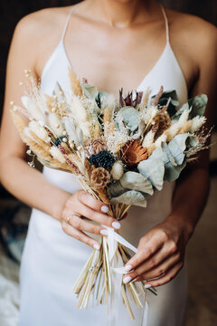 The bride holds in her hands a beautiful bouquet of dried flowers in the style of boho