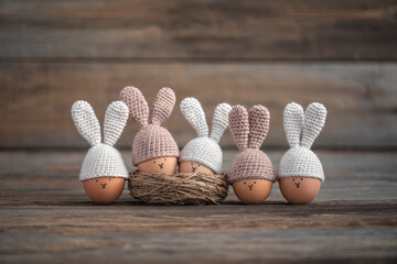 Five Easter eggs in crocheted hats with rabbit ears on a rustic wooden table. Soft focus.