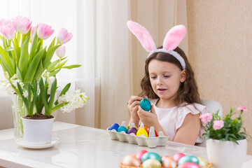 Cute little girl wearing bunny ears and drawing funny faces on Easter eggs.