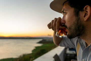 Closeup of a hipster at bar takes a shot of expensive rum during sunset