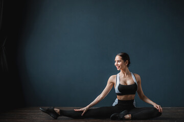 Obraz premium Fitness woman in sportswear doing stretching exercises, muscular model on dark