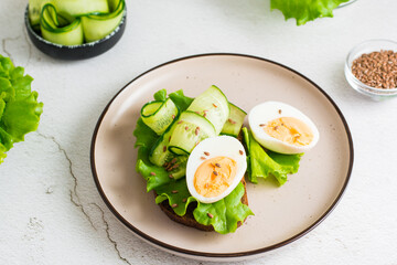 Ready to eat sandwich with rye bread, lettuce, cucumber, boiled egg and flax seeds on a plate on the table. Healthy eating on a diet. Close-up