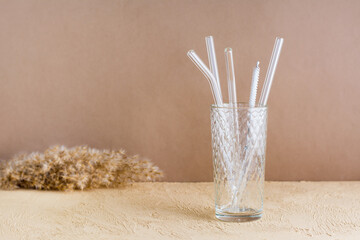 Glass reusable straws for drinks and cleaning brush in a glass on a beige textured background....