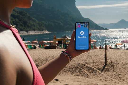 Girl on the beach holding a smartphone with OpenSea (online marketplace for NFT non-fungible tokens)  app on the screen. Rio de Janeiro, RJ, Brazil. March 2022
