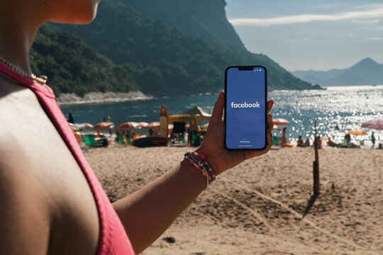 Girl on the beach holding a smartphone with Facebook app on the screen. Rio de Janeiro, RJ, Brazil. March 2022