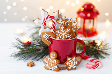 Hot winter drink in a red mug: cozy home composition with homemade gingerbread cookies, candy cane,...