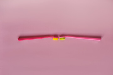 Two pink toothbrushes stand in pink glass on pink background. One brush is new and other has been used. Yellow bristles are disheveled, green bristles are new.