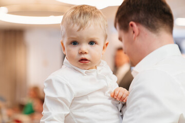 a dark-haired man holds a one-year-old boy in her arms. 