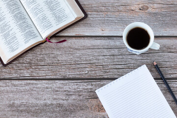Open Holy Bible Book with blank notebook, a cup of coffee, and pencil on a wooden table. Top view. Copy space. The biblical concept of morning Bible study from Scriptures inspired by God Jesus Christ.