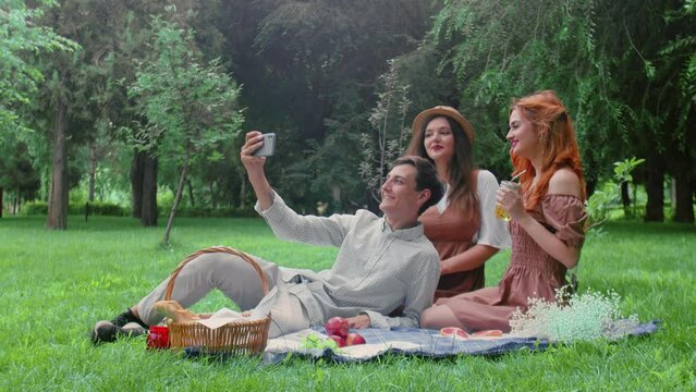 A guy and two girls are photographed on the phone at a picnic in the summer in nature