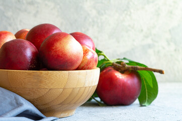 Fototapeta na wymiar Ripe fresh nectarines in wooden bowl on white stone background, healthy organic food, summer fruit