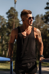 Cool athletic handsome guy with a haircut and sunglasses doing exercise and training workout outdoors