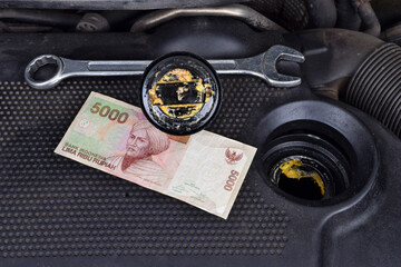 Indonesian rupiah money currency and the thick, greasy yellow motor oil under oil cap