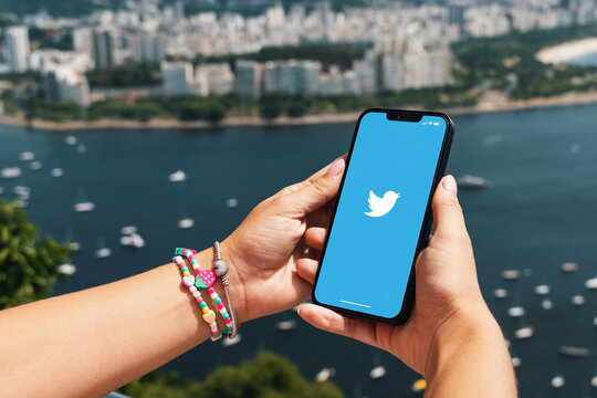 Girl holding smartphone with Twitter app on screen. City and bay with some boats in the background. Rio de Janeiro, RJ, Brazil. March 2022