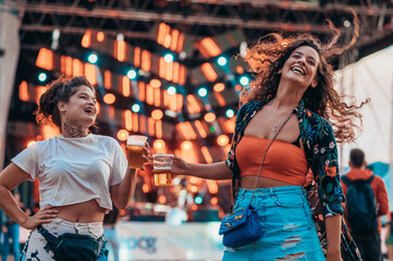 Two beautiful friends drinking beer and having fun on a music festival