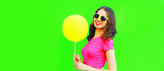 Portrait of happy smiling young woman with yellow balloon on green background