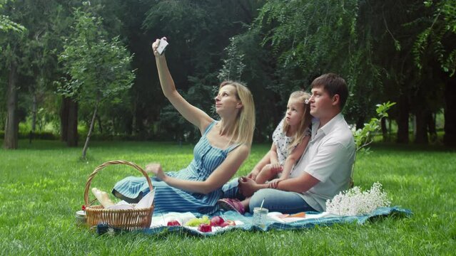 A woman takes pictures of herself, a child and a man at a summer picnic in nature