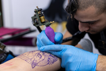 close-up of an alternative tattooist tattooing a client's skin with blue protective gloves in his small tattoo studio