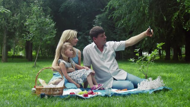 A man takes pictures of himself, a child and a woman at a summer picnic in nature