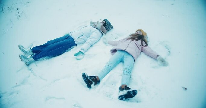 Young woman and daughter lie on ground making snow angels