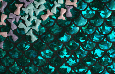 Colorful mermaid tails candies on a shiny green fabric © Venghaul