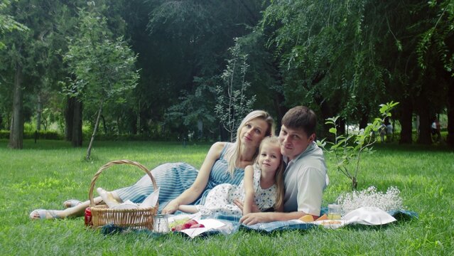The family lies on a blanket in nature in the summer and poses for a photo