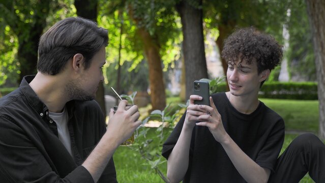 A guy takes pictures on the phone of another guy in nature in the summer. LGBT