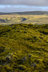An otherworldy, moss-covered lava field and a distant waterfall on the mountains near Kirkjubaejarklaustur, South Coast of Iceland