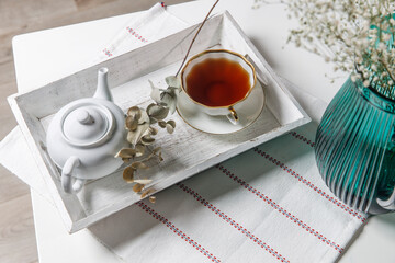 interior and home coziness concept. Top view. A cup of tea, a teapot with herbal tea, sugar bowl on a wooden white tray on the table. Porcelain cup