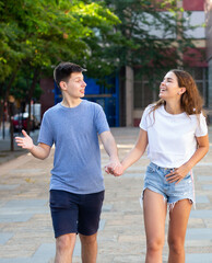 A couple of young people is walking on the street and holding hands