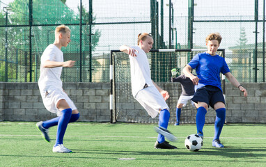 Game moments of football match between two teams of teenagers in white and blue shirts