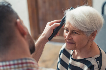 adult caucasian son taking care of his elderly mother by combing her short grey hair. High quality photo