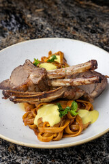 Costillas de cordero sobre pastas con salsa huancaína. Gastronomía peruana