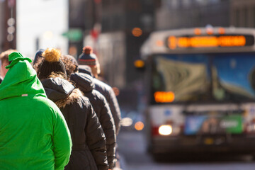 A person in a green outfit walking with a crowd down the street as a bus approaches.