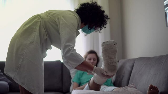 Smiling female doctor checking on a girl with a broken leg in plaster cast, female patient laying down in a hospital bed in pajamas