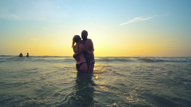 Happy cheerful young couple having fun in the sea at sunset, silhouette of couple enjoying together on a tropical beach on romantic vacation, honeymoon