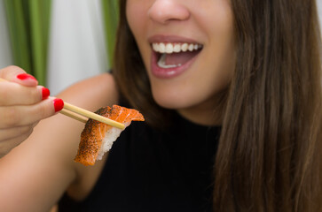 Woman eating delicious sushi, closeup on chopsticks.