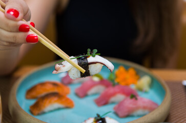 Obraz premium Woman eating delicious sushi, closeup on chopsticks.