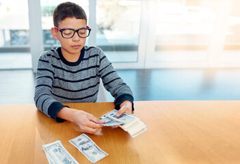 Saving up for the rainy days. Shot of a focused young boy counting his money on the dinner table at...