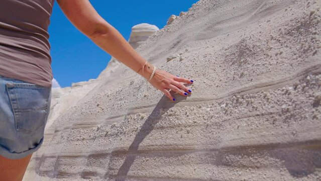 Slow motion close-up of a female sliding hand over a white rock formation showing strata layers on a sunny day in Milos, Greece