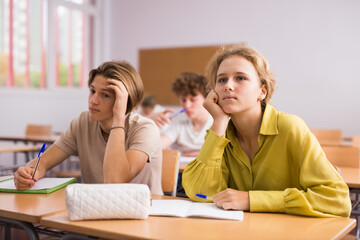 Fototapeta na wymiar Teenage girl and boy sitting together at desk and doing tasks in classroom.