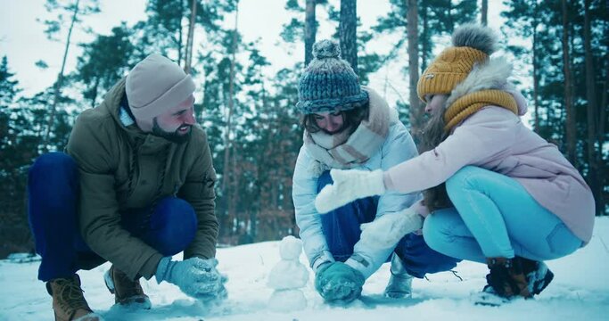 Young family makes small snowman on pine tree forest glade