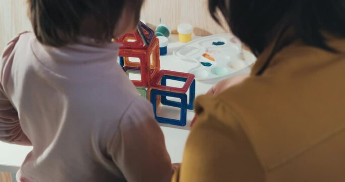 Child with his mother collects a magnetic constructor, a close up shot, a rear view, no faces are visible. The concept of development, joint family pastime and education of the child in a playful way