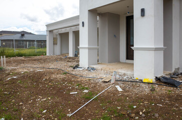 The construction site of a large residential suburban house with dirt and construction rubbish debris scattered about. Concept of self-build home, new house, and unfinished landscaping project.