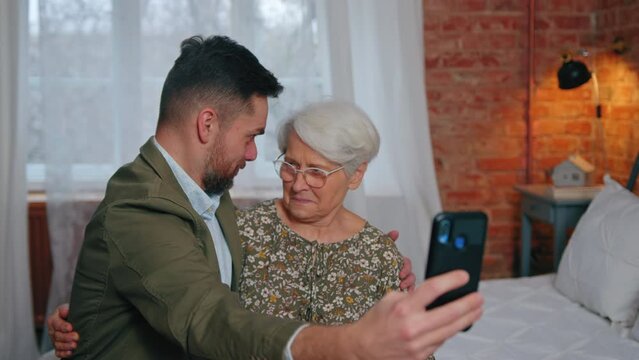 caucasian relatives sitting on a bed and making silly faces and taking selfies with a smartphone. High quality 4k footage