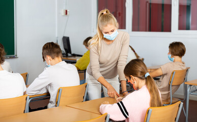Fototapeta premium Woman teacher in face mask explaining new theme to children during class in primary school indoors