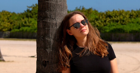 Young woman leaning against a palm tree at Miami Beach