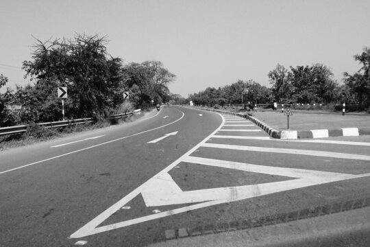 The white coloured markings on the Indian highway, black and white image shot in daytime.
