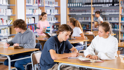 Obraz premium Cute tween girl and intelligent boy studying together in school library, reading books